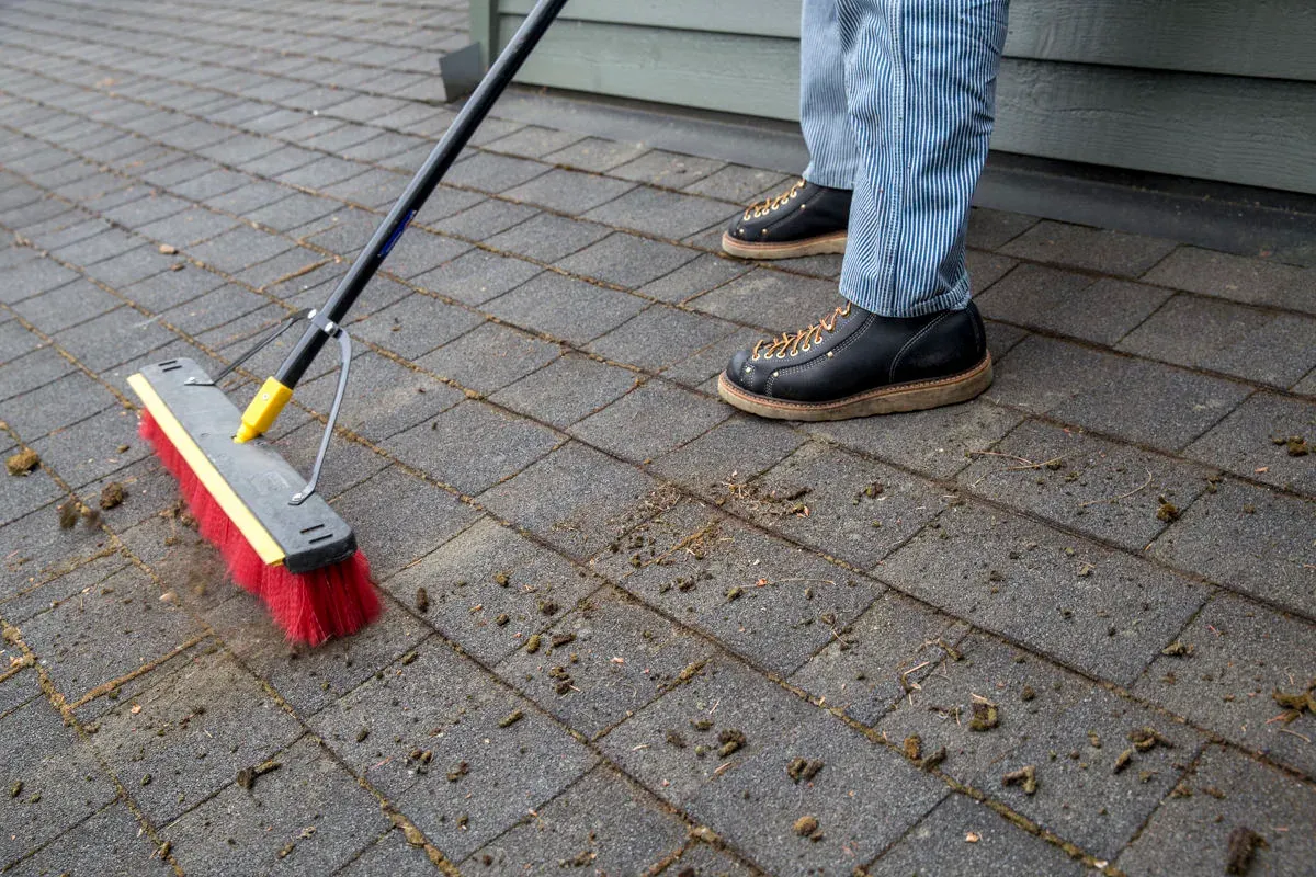 A long-handled brush sweeping loosened moss down a shingle slope