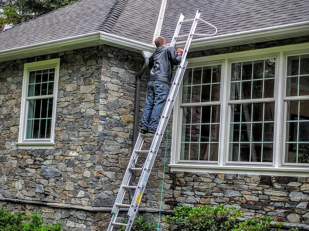 A ladder set at the eave of a house with the roof edge running away from it